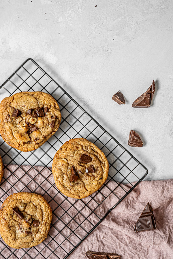 a cooling rack with chocolate chip cookies, pieces of chocolate scattered around