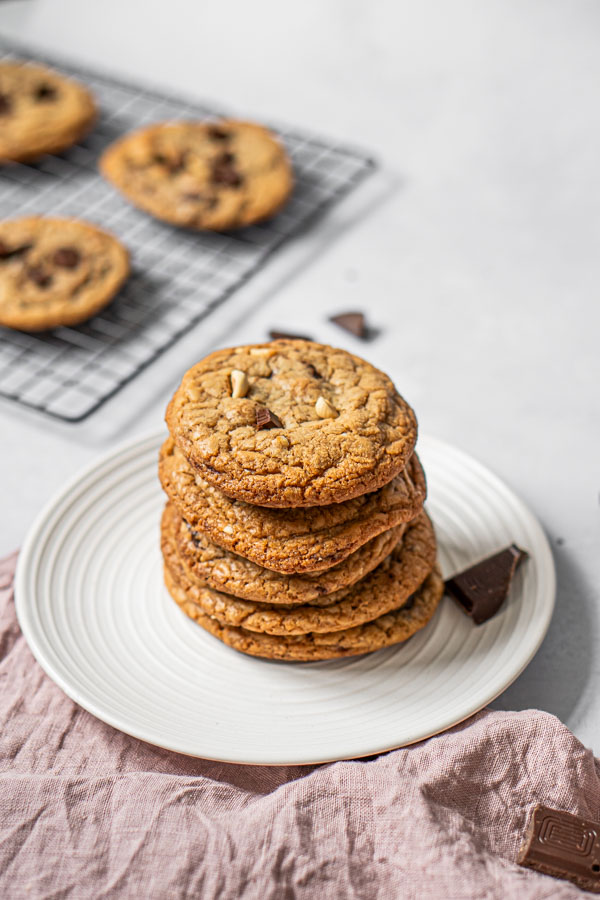 a pile of cookies on a plate on foreground, cooling rack with more cookies at the background