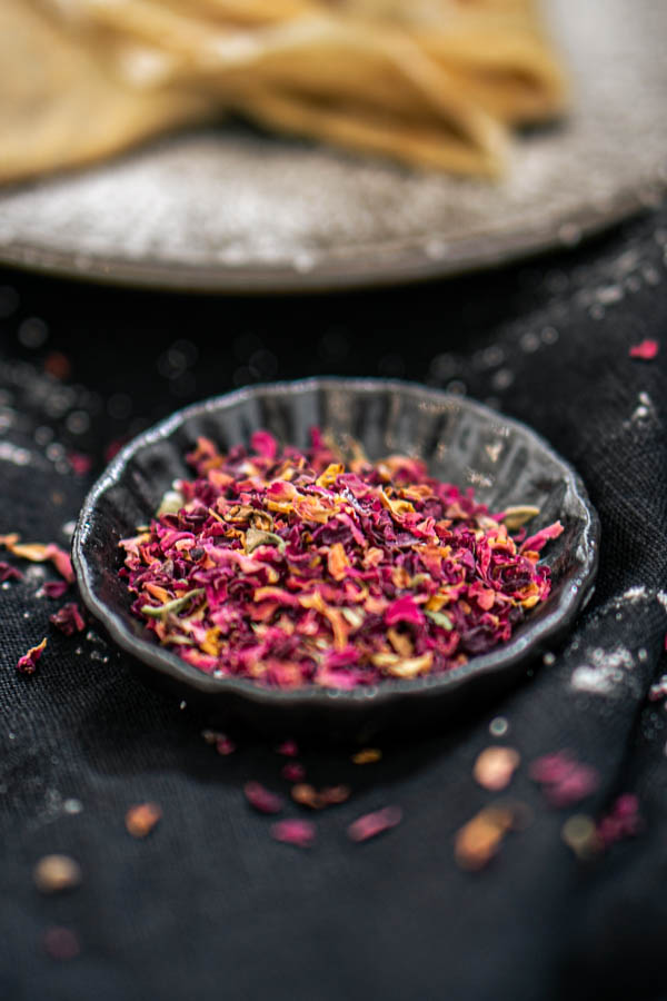 A picture of pinch bowl filled with rose petals. Plate with pancakes in the background.